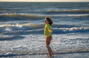 Çocuk yaz tatilinde sahilde koşuyor ve eğleniyor. Denizde oynayan mutlu çocuklar. Doğada denizli çocuklar. Deniz kıyısında tatilde deniz suyunda koşan mutlu çocuklar. Çocuk deniz sahilinde yürüyor.
