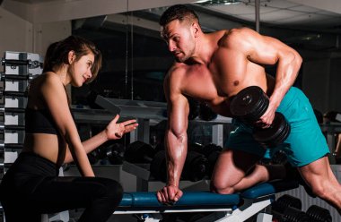 Spor salonunda kadınların dambıllarıyla egzersiz yapmasına yardım eden kişisel antrenör. Sporcu aile çiftleri konsepti. Çıplak karın kasları olan erkek sporcu. Güçlü atletik vücut