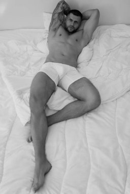 Genç ve seksi bir adamın yatakta yatışının en üst görüntüsü. Çıplak vücutlu, çıplak vücutlu, yakışıklı bir genç. Çıplak kaslı vücutla yatakta yatan kaslı genç bir adam. Seksi genç erkek model.