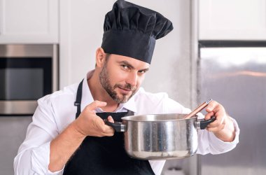 Erkek aşçı ya da aşçı mutfakta tencerede yemek pişiriyor. Gurme yemeği hazırlama süreci. Adam evde yemek pişiriyor, esrar kullanıyor. Şef yemek pişiriyor. Yakışıklı aşçı aşçı konsepti