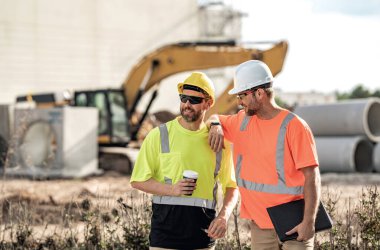 Kasklı iki inşaat işçisi dışarıda çalışıyor. İnşaat işçileri inşaat alanında çalışıyor. İnşaat işçisi olmak çok fazla fiziksel güç gerektirir.