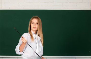 Genç sarışın öğretmen dersi işaret ediyor. Kara tahtanın yanında işaretçi öğretmenliği yapan sevimli genç bir kadın.