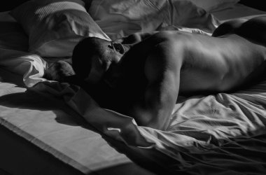 Handsome muscular man lying shirtless in bed. Young handsome man resting on the bed at home. Guy with thletic flexing muscles. Sexy young handsome naked man on bed. Seductive gay