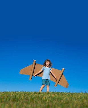 Mutlu çocuk yaz mevsiminde gökyüzü arka planında oyuncak kanatlarla oynuyor. Çocukların başarısı, lideri ve kazanan konsepti.