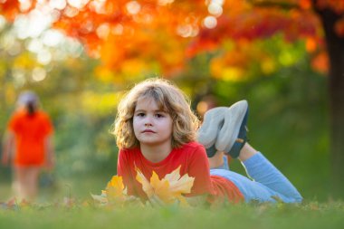 Sonbahar. Sonbahar parkındaki yaprakların üzerine uzanmış çocuklar. Sonbahar yapraklarında yatan çocuk. Sonbahar yaprakları konsepti. Parkta yapraklarla oynayan çocuk.