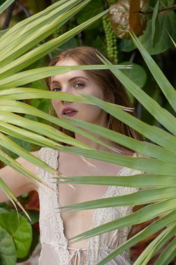 Yüzünde palmiye yaprağı olan güzel bir kadının portresi. Genç, güzel bir kadın yüzü. Genç ve güzel bir kadın. Yaz suratı. Summer Cilt Bakımı. Doğada güzel bir kadın. Yaz yüzü kozmetik egzotik konsepti