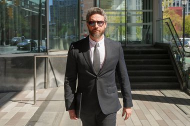 Modern ofis binasının önünde duran yaşlı bir iş adamı. İş başarısı. Dışarıyı düşünen bir iş adamı. Takım elbiseli modern iş adamı ofis manzarasının yanında duruyor.