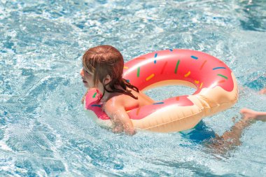 Çocuk plajda ya da havuzda rahatlar. Yüzme havuzunda yüzen bir çocuk. Çocuklar yaz tatili ve tatil konsepti. Yüzme havuzunda renkli yüzüklü mutlu küçük çocuk.