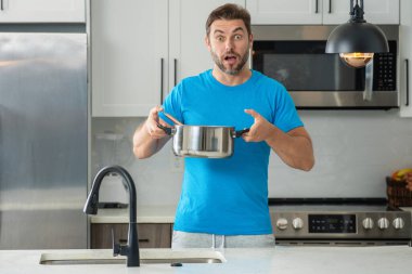 Mutfakta yemek yapan adam. Yakışıklı adam Modepn mutfağında lezzetli yemekler hazırlıyor. Erkek aşçı mutfakta yemek pişiriyor. Milenyum adamı mutfağın arka planında sağlıklı bir yemek hazırlıyor. Mutfak aletleri