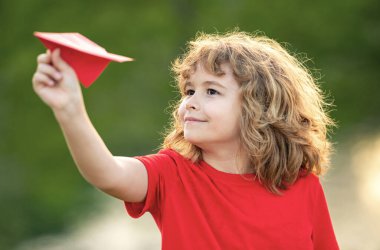 Mutlu çocuk kağıt uçak tutuyor. Oyuncak uçak çocukların elinde. Mutlu çocuk eğiliyor ve sarı kağıt uçak fırlatıyor. Çocuk kağıt uçakla oynuyor. Kağıt uçakla oynayan çocuk