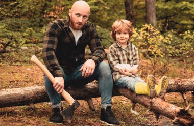 Baba ve oğlu orman ormanlarında gezintiye çıktılar. Babası dışarıda olan sevimli bir çocuk. Yakışıklı genç baba ve oğlu baltayla odun kesiyor.