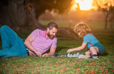 Dışarıda mutlu bir aile. Baba ve oğul sonbahar bahçesinde satranç oynuyorlar. Aktif insanlar parkta satranç oynayıp eğleniyorlar, çocuklarla vakit geçiriyorlar.