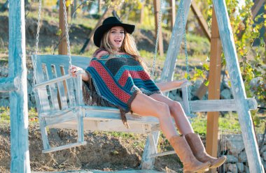 Parkta salıncakta sallanan boho tarzı genç bir kadın. Güzel hippi kadın bahçede salıncakta dinleniyor. Şapkalı şehvetli bir kızın yaz moda portresi. Gülümseyen mutlu bir kızın açık hava portresi
