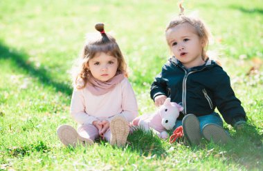 Yeşil çimenlerde oynayan bir bebek. Çocuk yaz bahçesinde aile pikniğinde eğleniyor. Erkek ve kız kardeş yeşil bir çayırda birlikte oynuyorlar. Mutlu çocuklar bahar parkında yeşil çimlerde oturuyor.