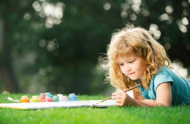 Çocuk açık havada parkta resim çiziyor.