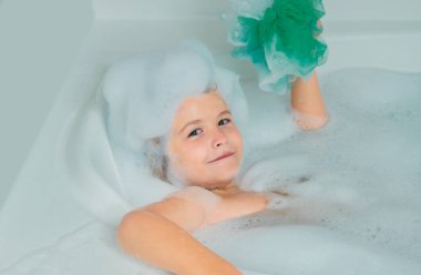 Islak kıvırcık saçlı komik çocuk mutfak lavabosunda bol köpüklü banyo yapıyor.