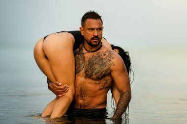 Man carrying booty woman in bikini. Sexy butt. Summer sexy models. Embracing love couple. Summer couple in love. Sexy couple in love having holidays on the sea in summer. Passion couple in the sea