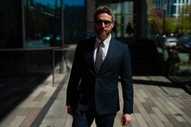 Modern ofis binasının önünde duran ciddi bir iş adamı. İş başarısı. Dışarıyı düşünen bir iş adamı. Takım elbiseli modern iş adamı ofis manzarasının yanında duruyor.