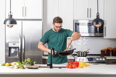 Aşçı mutfakta tavayla yemek pişiriyor. Şef aşçı tavayla hazırlar. Aşçı modern mutfakta tavayla yemek pişiriyor. Olgun aşçı adam mutfakta durup yemek hazırlıyor.