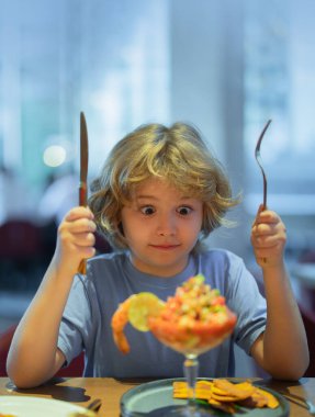 Funny surprised Little boy eating seafood in cafe. Kid eat Food fish gourmet seafood shrimp in restaurant. Adorable little boy at restaurant having breakfast