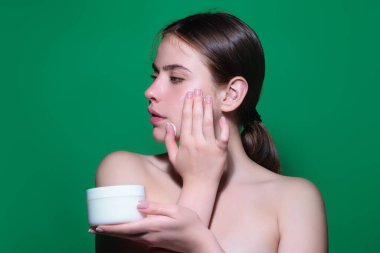 Yüzüne krem süren genç bir kadın. Cilt bakımı ve kozmetik konsepti. Cilt bakımı. Stüdyo geçmişine krem süren bir kız. Cilt nemlendirici