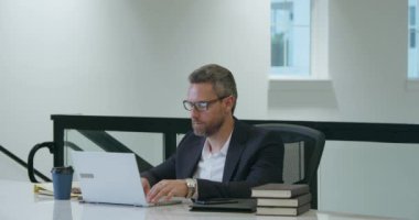 Orta yaşlı iş adamı ofiste dizüstü bilgisayarla çalışıyor. İspanyol iş adamı dizüstü bilgisayar kullanıyor. Milenyum adamı iş yerinde dizüstü bilgisayar kullanıyor. Genel müdür, ofis çalışanı, ofiste çalışan iş adamları.