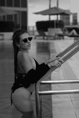 Lüks havuzdaki moda kadını. Yüzme havuzunun yanında bronzlaşmış ince vücutlu beyaz bikinili zarif seksi kadın. Zengin yaz uykusu