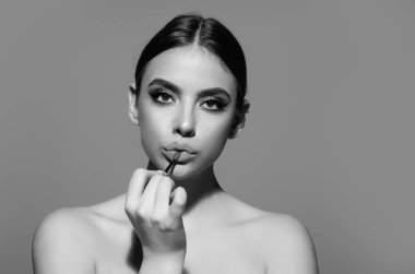Gorgeous young woman in stylish makeup. Girl posing with new lipstick in studio. Sexy girl rouging her lips. Sexy model holding red lipstick. Applying lipstick cream balm to mouth. Red is trending