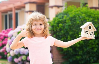 Mutlu çocuk yeni evine karşı oyuncak evi elinde tutuyor. Çocuklar için konut kavramı