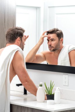 Bin yıllık İspanyol adam aynaya, yüz derisine ve sakalına bakıyor. Erkek güzellik ürünleri. Cilt bakımı, spa. Güzel bir adamın güzel portresi. Spa modeli, nemlendirici krem