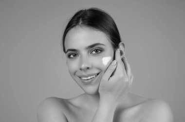 Beautiful model applying cosmetic cream treatment on face. Facial treatment. Beauty portrait of young topless woman with bare shoulders applying face cream