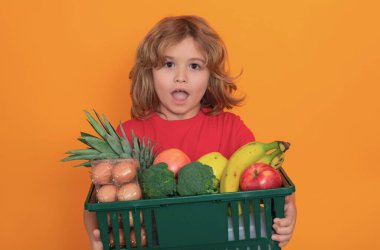 Market alışverişi. Sevimli çocuk alışveriş arabası ağzına kadar yiyecek dolu. Çocuk alışveriş sepetini sarı arka planda tutuyor. Mağaza, alışveriş, satış ve indirimler