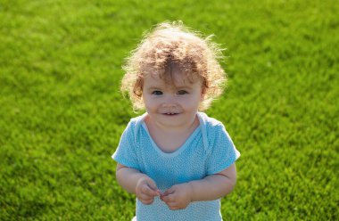 Güneşli yaz akşamında çimlerin üzerinde mutlu bir bebek. Dışarıda gülümseyen bir çocuk. Bebek yüzü yakın plan. Komik küçük çocuk, yakın plan portre. Sarışın çocuk, gülümseyen duygusal yüz.