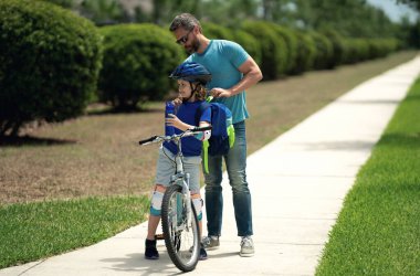 Baba oğul kavramı. Baba oğluna bisiklet sürmeyi öğretiyor. Baba oğlunun Amerikan mahallesinde bisiklet sürmesine yardım ediyor. Kasklı çocuk babasıyla bisiklet sürmeyi öğreniyor. Babalar Günü