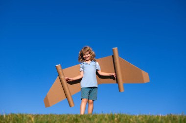 Seyahat hayalleri. Arka planda oyuncak uçakla jetpack üzerinde uçan bir çocuk. Mutlu çocuk karton uçakta oynuyor. Çocuk dışarıda eğleniyor.