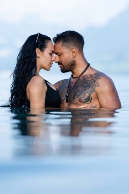 Sensual Couple in love embracing each other in water. Romantic couple kissing in the sea. Sexy couple hug on the summer beach. Love and romance couple. Muscular Hispanic man and woman in love clipart