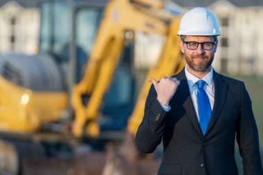 Başarılı bir inşaat işletmesi sahibi. Kazıcının yanındaki kask ve takım elbiseli inşaat işçisi. İnşaat alanının önünde kendine güvenen bir inşaat sahibi. İnşaat mühendisi.