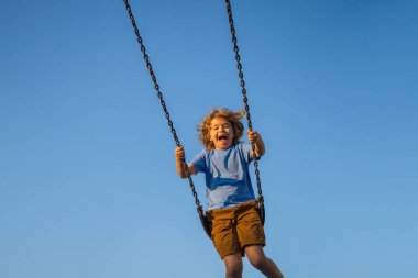 Zincirle sallanan çocuk şehir çocuklarının oyun alanında sallanıyor. Sallanma turu. Salıncakta salıncakta sallanan tatlı bir çocuk. Çocuklar parkta oynuyor. Sarışın küçük oğlan çocuk parkında sallanıyor.
