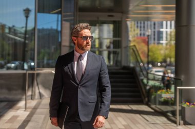 Modern ofis binasının önünde duran yönetici bir iş adamı. İş başarısı. Dışarıyı düşünen bir iş adamı. Takım elbiseli modern iş adamı ofis manzarasının yanında duruyor.