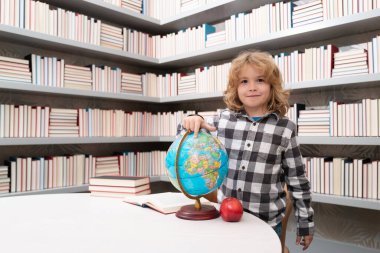 Okul ve öğrenciler sınıfta. Eğitimli çocuklar. Okul sınıfındaki zeki çocuk öğrenci seni. Okuma ve öğrenme konsepti. Okul çocuğu kütüphanede, okul malzemelerinin yanında. Çocuk coğrafya öğreniyor