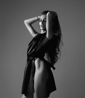 Seductive sexy lovely attractive young sensual woman in fashion black dress and perfect slim body posing on gray studio background. Beautiful elegant fashion model, studio portrait. Beautiful face