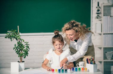 Kid drawing with teacher. Children from elementary school study at draw lesson. Pupil with teacher painting. Education and knowledge