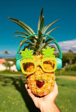 Yaz tropik ananas arka planı. Ananas güneş gözlüklü, mavi gökyüzü arka planında bir palmiye ağacının altında. Plajda kokteyl partisi, dinlenme, rahatlama ve yaz konsepti.