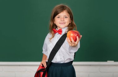 Okuldaki sevimli çocuk. Sınıftaki kırmızı elmalı çocuk kara tahtanın arkasında. Eğitim, öğrenme ve çocuk kavramı
