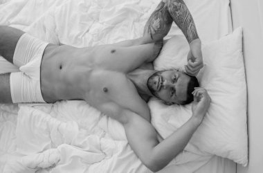 Young sexy man lying on a bed. Handsome young man with naked body, bare torso, undressed. Muscular young man laying on bed with naked muscular body. Sexy young male model