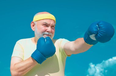 Boks pozisyonunda kıdemli sporcu boks eldivenleriyle egzersiz yapıyor. Aktif boş zaman. En iyi kardiyo çalışması