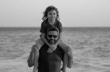 Baba ve oğul gün içinde plajda yürüyorlar. Arkadaş canlısı bir aile. Babalar Günü. Aşk ailesi, baba ve oğlu sahilde deniz doğasında birlikte yürürler. Oğullar babalarının omuzlarına biner.