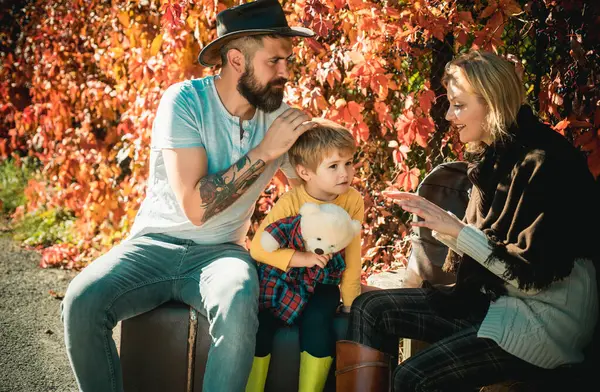 stock image Sensual family photo at autumn park. Bearded tattoed man in hat, charming blonde woman and little kid in season cozy clothing. Baby boy walking with parents at fall autumnal garden