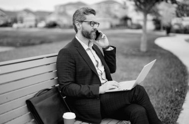 İş konuşmaları. İş adamı telefonda konuşuyor. Parktaki bankta oturuyor. Takım elbiseli adam dışarıdaki telefonu arıyor. Yakışıklı iş adamı telefonda konuşuyor. Park bankında otur. Takım elbiseli bir iş adamı parkta telefonda konuşuyor.