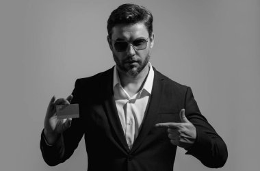 Stüdyonun gri arka planında kredi kartı tutan bir iş adamı. Kredi kartı olan bir iş adamı, banka indirimi öneriyor. E-bankacılık, e-ticaret, para transferi için kredi kartı